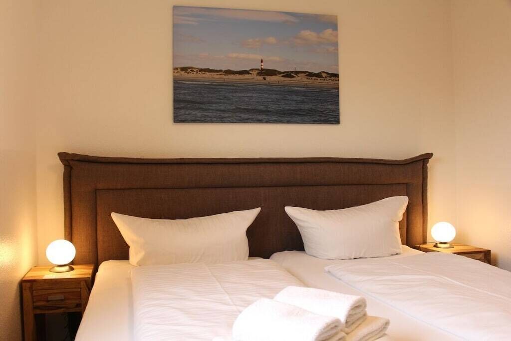 A neatly made bed with white linens and pillows, a headboard, and a nightstand with a lamp.