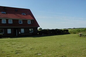 A red-roofed building with a grassy yard and a hedge in the foreground. - Holiday home in Dorum with swimming pool (Dorum)