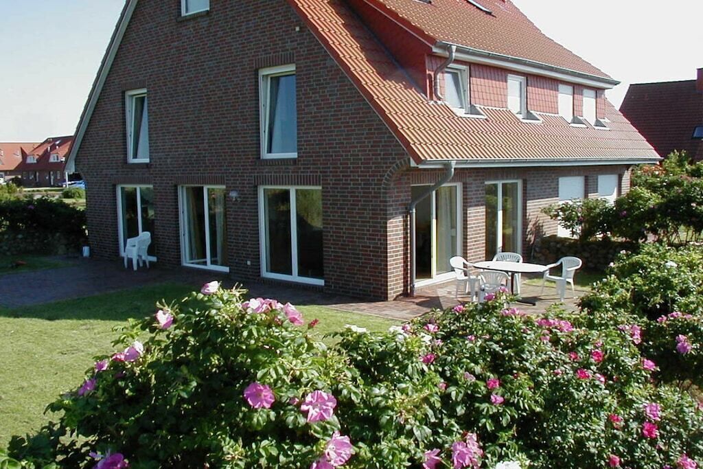 A two-story brick house with a sloped roof, large windows, and a patio with outdoor furniture.