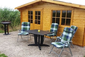A wooden cabin with a table and four chairs, a small table with a bottle, and a window with a view of the surrounding area. - Holiday home in Dorum with swimming pool (Dorum)