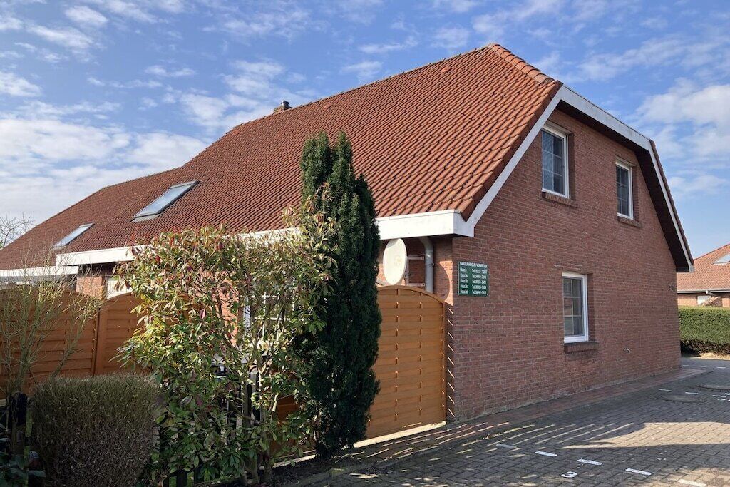 A two-story house with a sloped roof, a wooden fence, and a garden.