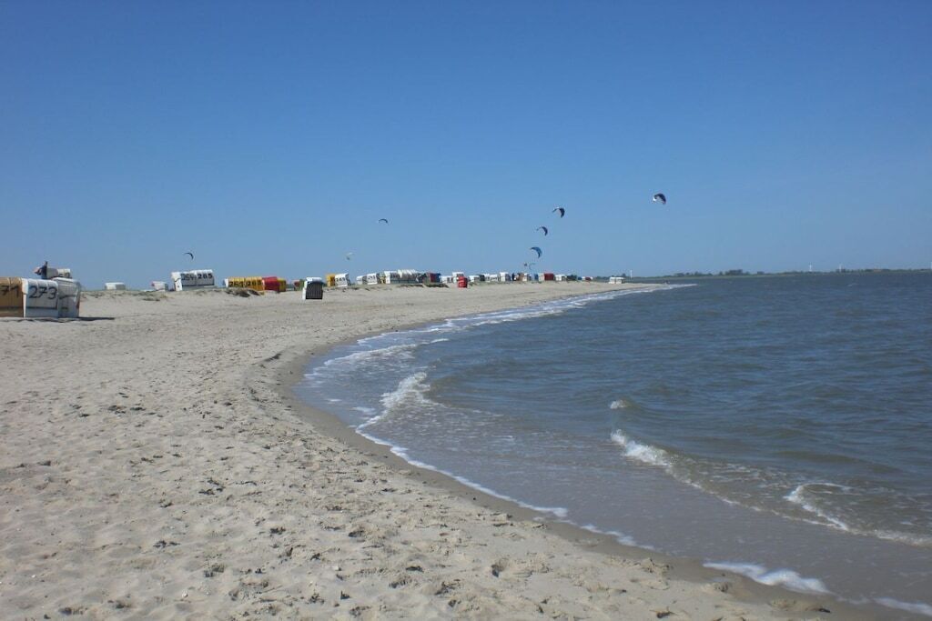 Een strand met een zandrijk strand, een rustige zee, en diverse tenten op de achtergrond.