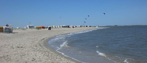 A beach with a sandy shore, a calm sea, and several tents in the background.