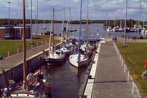 A marina with boats docked, a pedestrian walkway, and a building in the background. - Holiday home in Hooksiel with swimming pool (Hooksiel)