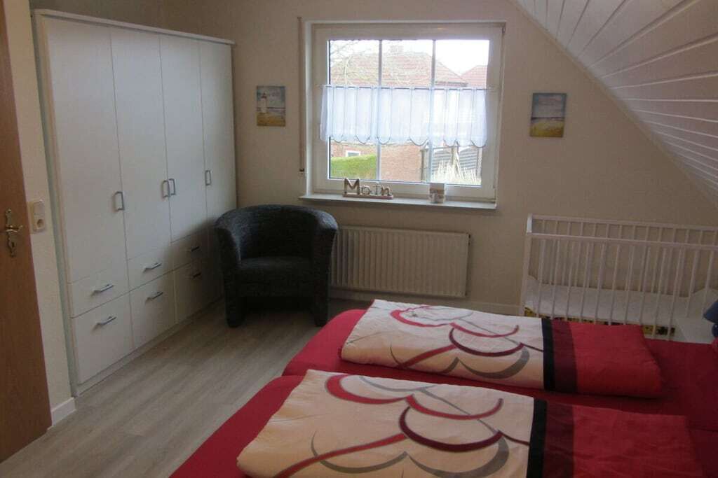 Quarto com guarda-roupa, radiador, janela com cortinas e cama com roupa de cama estampada.