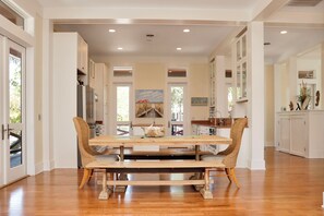 Una cocina amplia con una isla central, muebles blancos y una zona de comedor con mesa de madera y sillas de mimbre.