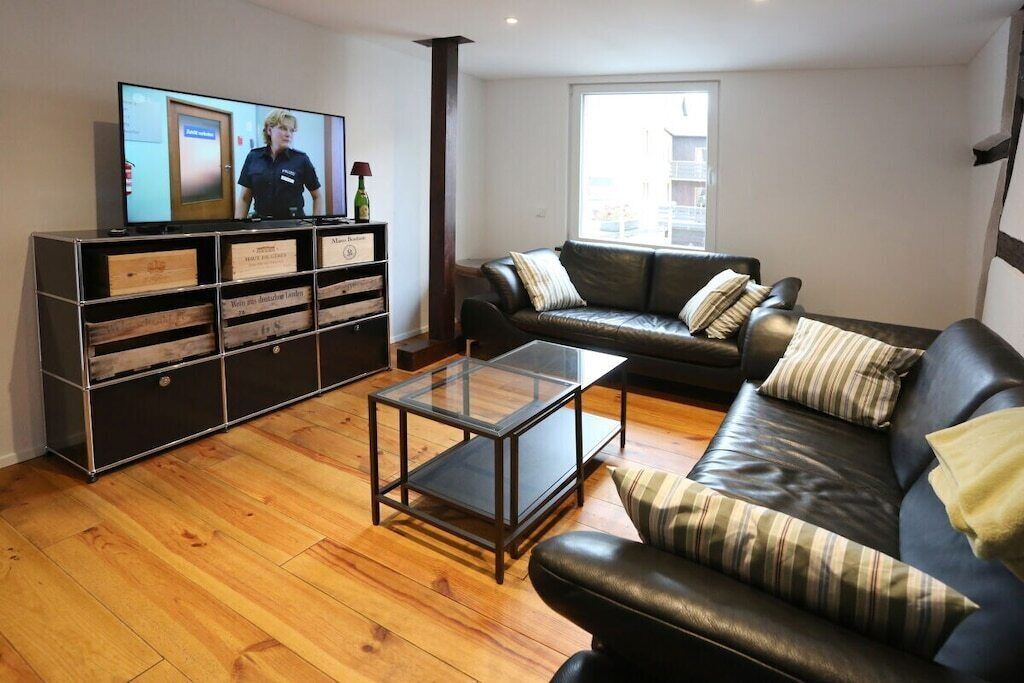 Un salon avec un canapé en cuir, une table basse en verre, un téléviseur posé sur un meuble et un buffet en bois doté de tiroirs.