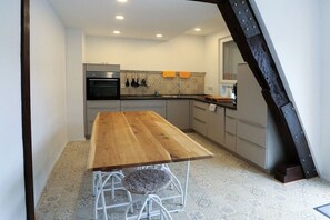 A kitchen with a wooden table, a built-in oven, and a tiled backsplash. - Quartier Blanc de Noir (Reil)