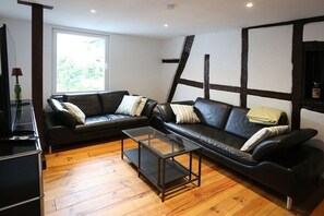 A modern living room with two black leather sofas, a glass coffee table, and wooden flooring. - Quartier Blanc de Noir (Reil)