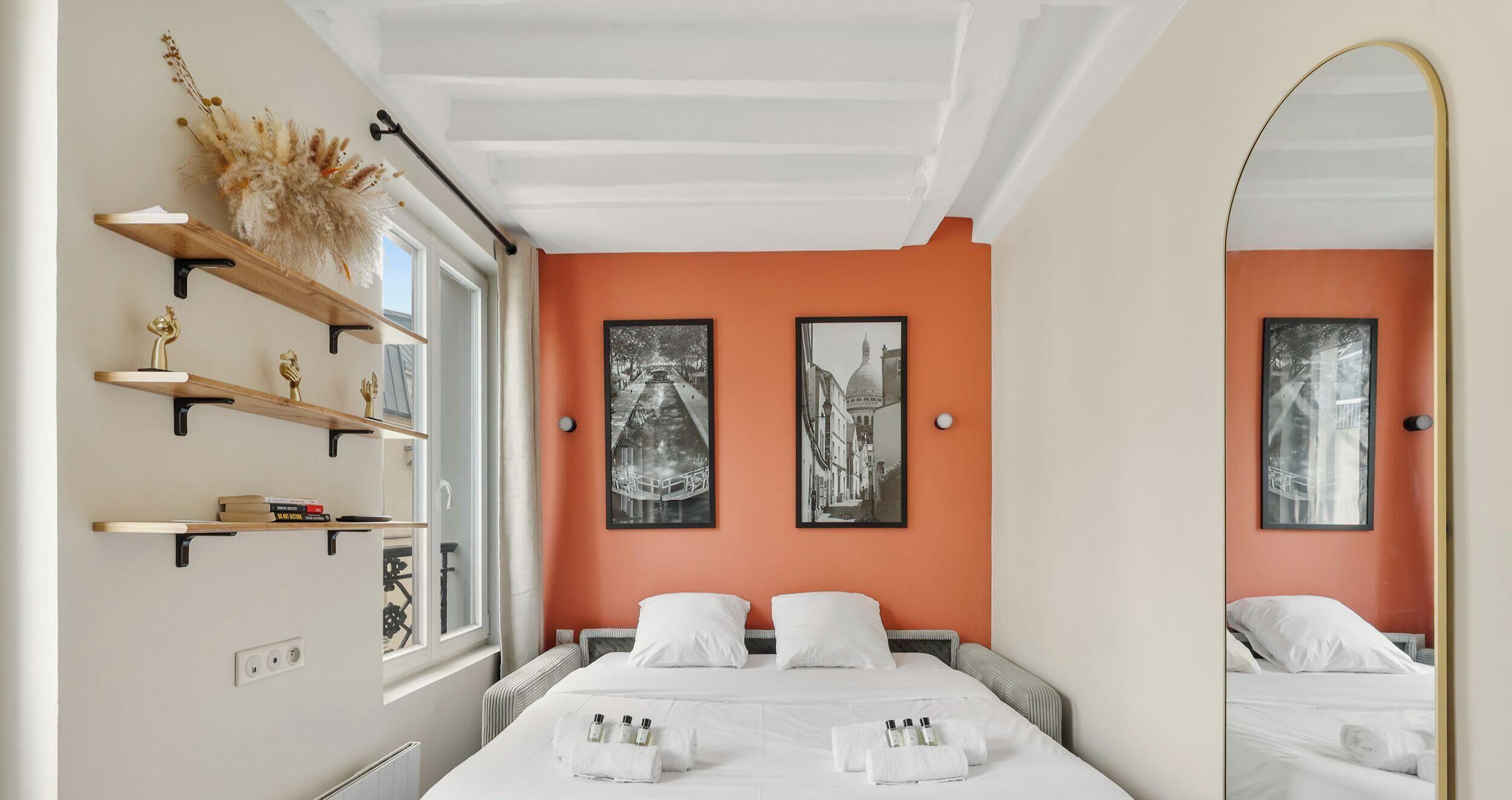 Een hotelkamer met een bed, twee nachtkastjes, een raam, een spiegel en kunst aan de wanden.