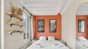 Hotellihuone, jossa on sänky, kaksi yöpöytää, ikkuna, peili ja taideteoksia seinillä.