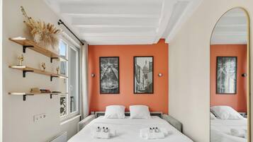Een hotelkamer met een bed, twee nachtkastjes, een raam, een spiegel en kunst aan de wanden.