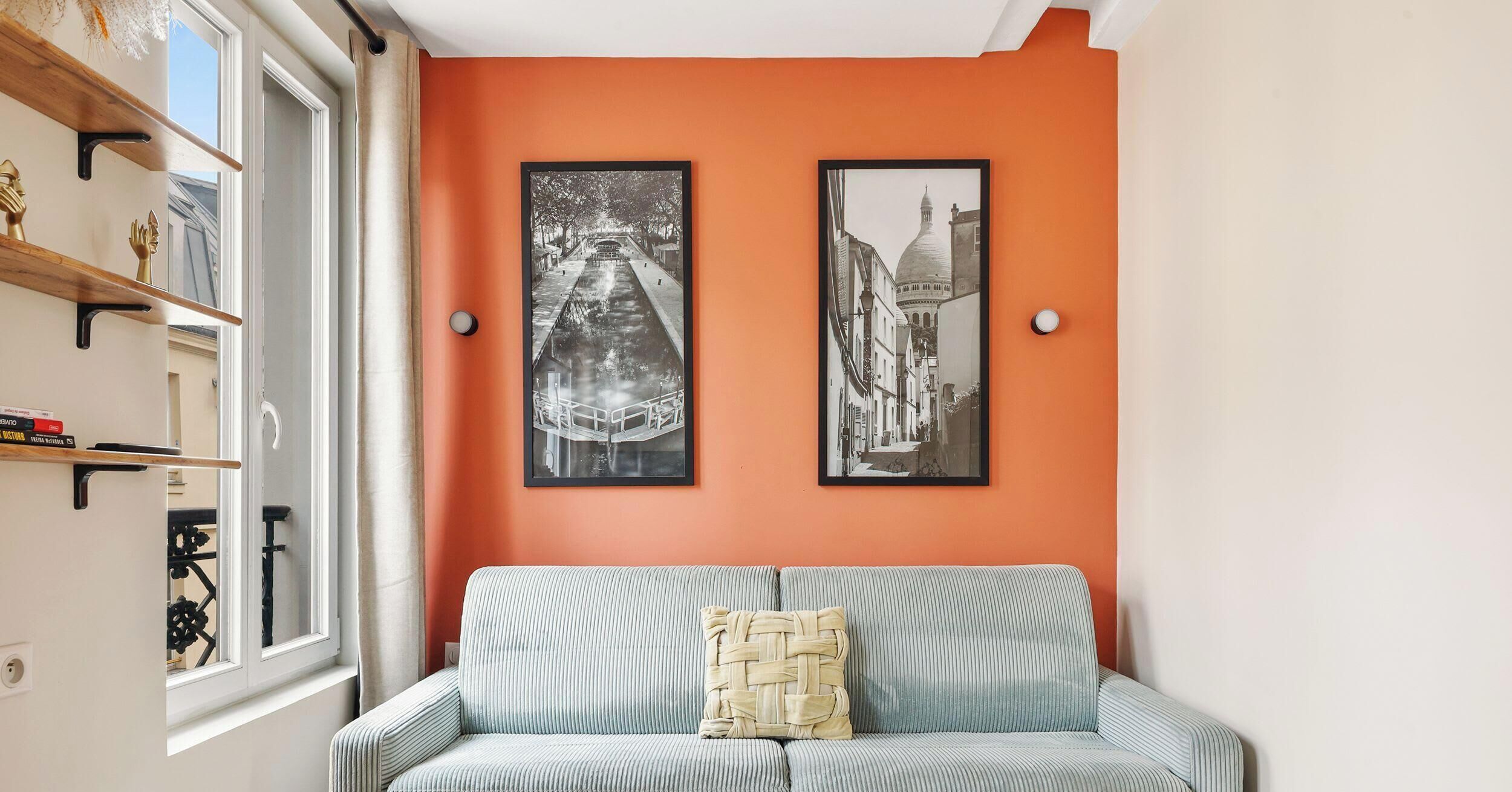 Een kamer met een bank, twee ingelijste foto's aan de muur en een raam met uitzicht.