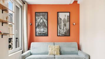 Een kamer met een bank, twee ingelijste foto's aan de muur en een raam met uitzicht.