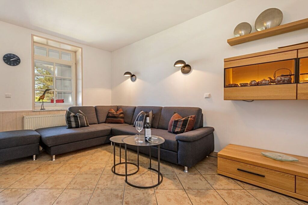 Ein modernes Wohnzimmer mit einem Ecksofa, einem kleinen runden Tisch und einer Holzkommode mit Dekoration.