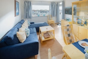 Sala de estar com sofá, mesa pequena, armário de madeira e vista para o exterior.