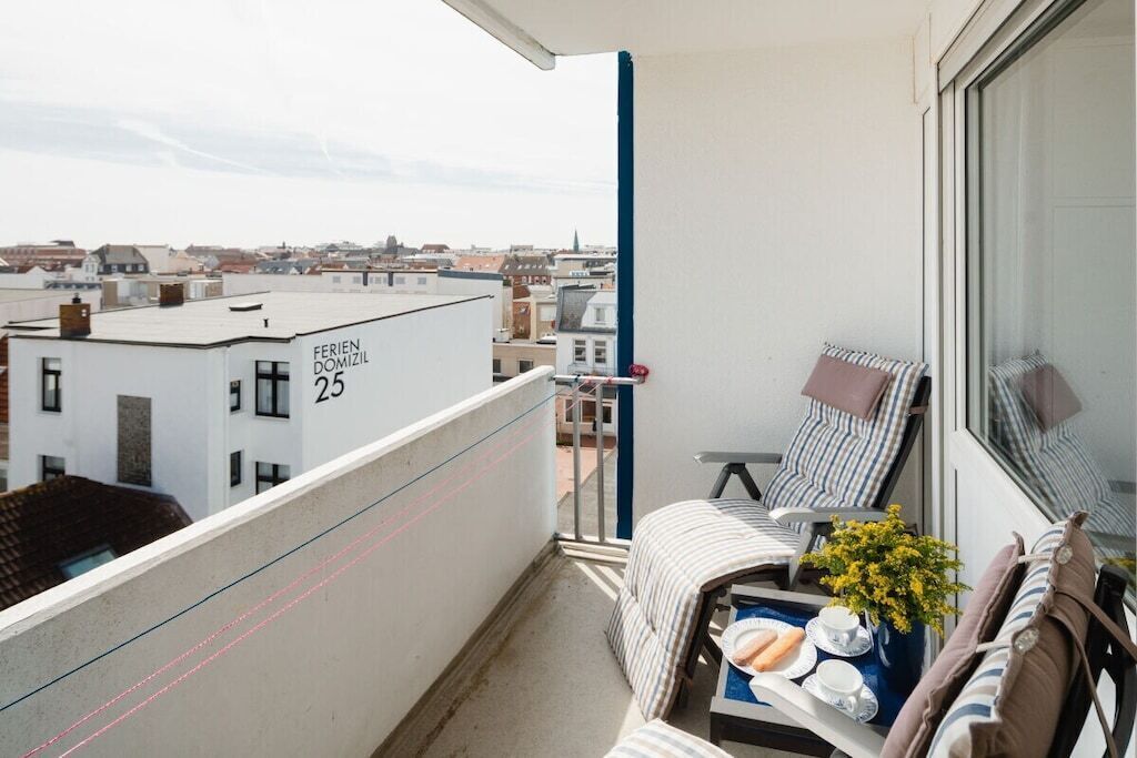 Ein Balkon mit Blick auf die Stadt, ein Stuhl, ein kleiner Tisch mit Tablett und ein Gebäude mit der Aufschrift 'FERIEN DOMIZIL 25'.