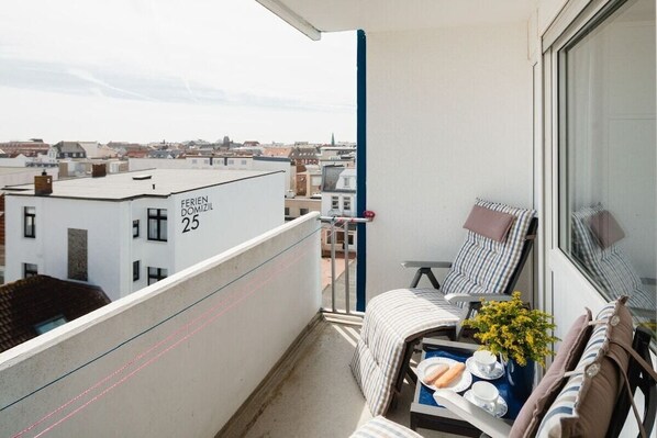 Un balcon avec vue sur la ville, une chaise, une petite table avec un plateau, et un bâtiment portant l’inscription « FERIEN DOMIZIL 25 ».