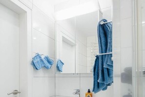 Une salle de bain avec des carreaux blancs, un miroir, un porte-serviettes avec des serviettes bleues et un flacon de savon.