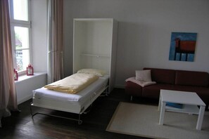 Habitación con una cama individual, un sofá, una mesita y una ventana con cortinas.
