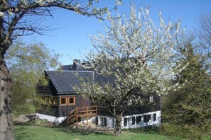 A two-story house with a wooden staircase leading to a balcony, surrounded by greenery and a clear sky. - Holiday apartment with 1 bedroom (Rechenberg-Bienenmühle)