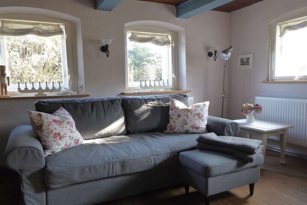Un canapé gris agrémenté de coussins à motifs floraux, une petite table sur laquelle est posé un vase, et un lampadaire.