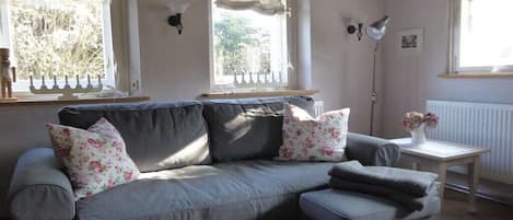 A grey sofa with floral cushions, a small table with a vase, and a floor lamp.