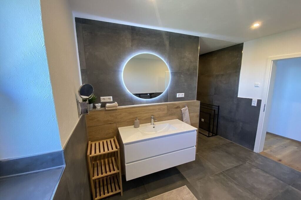A modern bathroom with a large mirror, a white sink, and a wooden vanity.