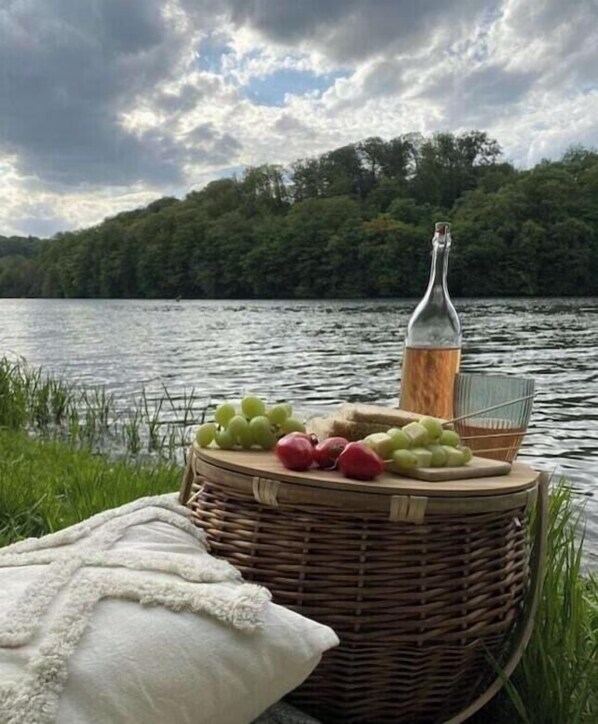 En korg av rotting med frukt och en flaska, placerad vid en sjö.