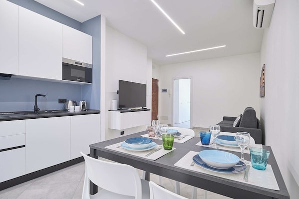 A modern kitchen with white cabinets, a built-in oven, and a dining area with a table set for two. - Casa Maggie (Albenga)