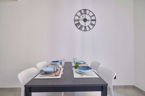 Una mesa de comedor con un reloj en la pared, sillas blancas y platos azules y verdes.