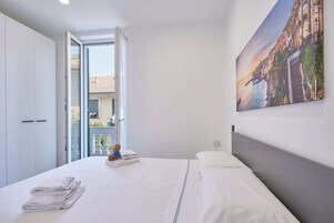 A bedroom with a bed, a painting, a window, and a door.