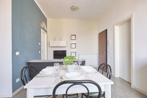 Un comedor con una mesa preparada para cuatro, sillas, una planta en maceta y un televisor en la pared.