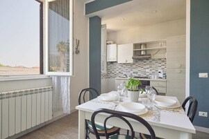 A dining area with a table set for two, a potted plant, and a view of the kitchen.