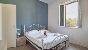 Un dormitorio con una cama individual, una mesita de noche, una ventana con cortinas y vistas a árboles.