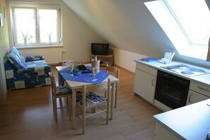 A compact living space with a dining table, chairs, a sofa, a television, and a kitchen area with an oven. - Holiday apartment with 1 bedroom (Eichstetten am Kaiserstuhl)