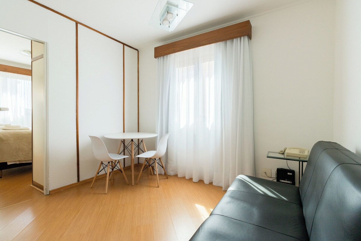 Ein modernes Wohnzimmer mit einer Couch, einem Esstisch mit Stühlen und einem großen Fenster mit Vorhängen.