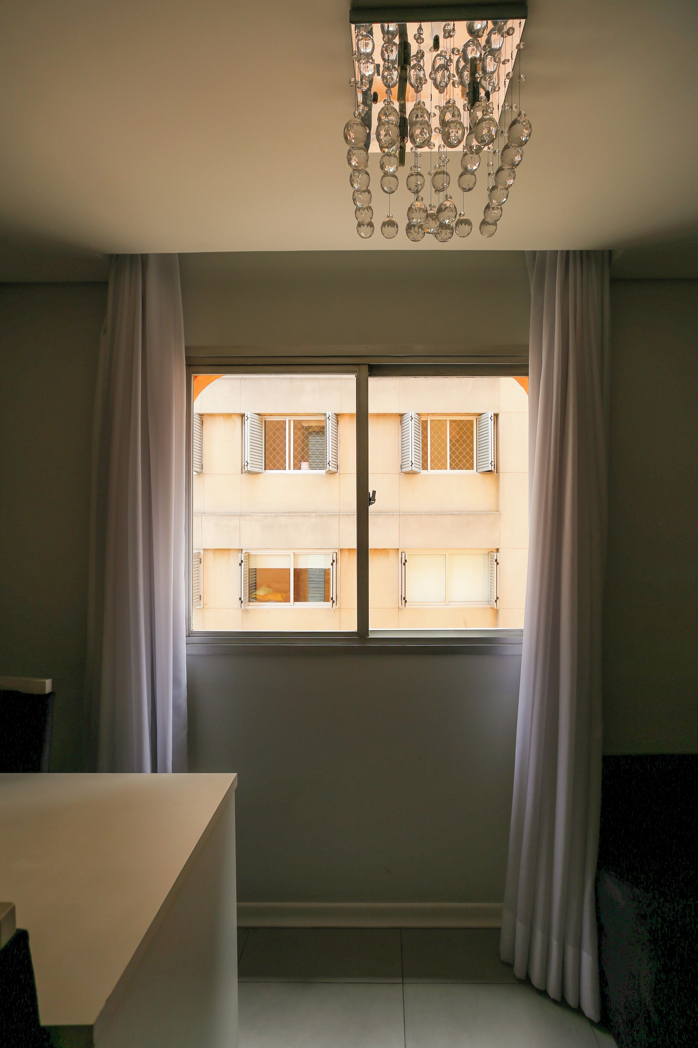 Una stanza con una grande finestra, tende bianche e un lampadario.