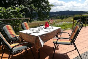 Ein Patio-Garnitur mit Stühlen, eine rote Vase und Blick auf eine grüne Landschaft.