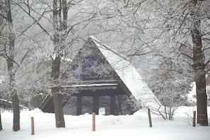 Eine verschneite Holzhütte mit Satteldach, umgeben von kahlen Bäumen und einem mit Schnee bedeckten Boden.