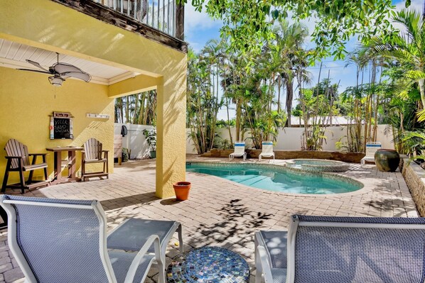 Ein Poolbereich mit Liegestühlen, einem Deckenventilator und einer Terrasse mit Topfpflanzen.
