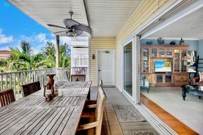 Eine Holzterrasse mit Tisch und Stühlen, einem Deckenventilator und einer Glasschiebetür, die zu einem Wohnbereich mit Fernseher und Holzschränken führt.