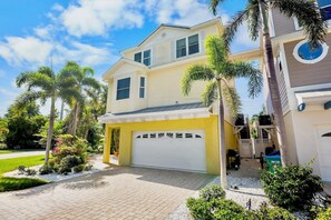 A two-story house with a garage, surrounded by palm trees and a well-maintained lawn. - Villa Sand Dollar by Anna Maria Vacations (Holmes Beach)