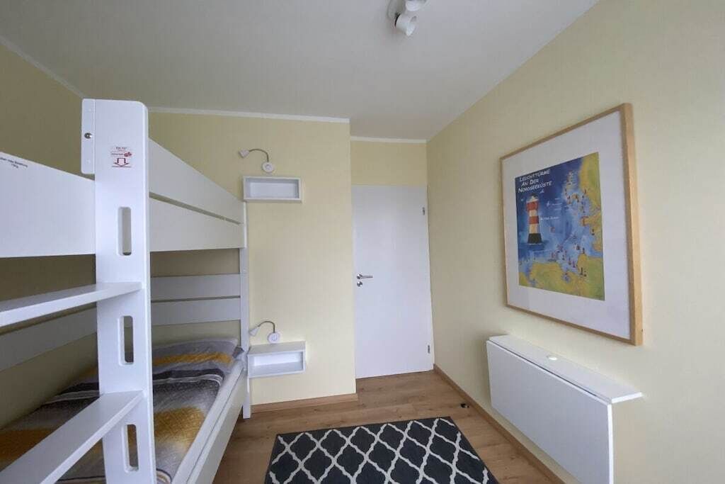 Una habitación con literas, una mesita de noche pequeña, un radiador y un mapa enmarcado en la pared.
