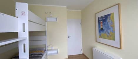 Ein Zimmer mit Etagenbetten, einem kleinen Nachttisch, einem Heizkörper und einer gerahmten Karte an der Wand.
