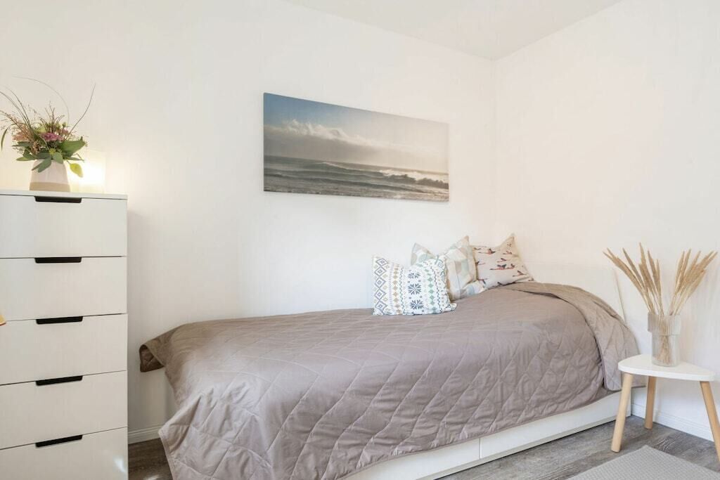 Un dormitorio con cama, cómoda, un cuadro y un florero con plantas.