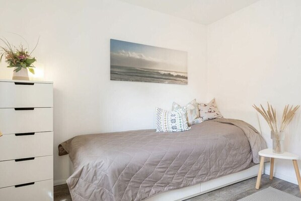 A bedroom with a bed, a dresser, a painting, and a vase with plants. - Holiday apartment with 1 bedroom (Fehmarn)