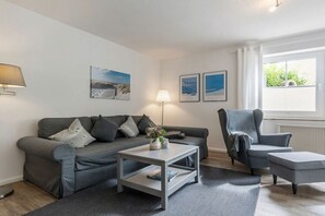 Un salon moderne avec un canapé gris, un fauteuil assorti, une table basse et une lampe. Deux tableaux encadrés sont accrochés au mur.