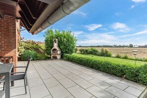 Een terras met een bakstenen muur, een stenen buitenoven en een tafel met stoelen.