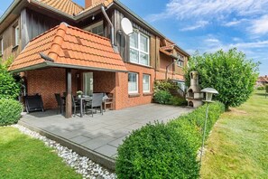 Een twee verdiepingen tellend huis met een bakstenen gevel, een pannendak en een patio met een tafel en stoelen.